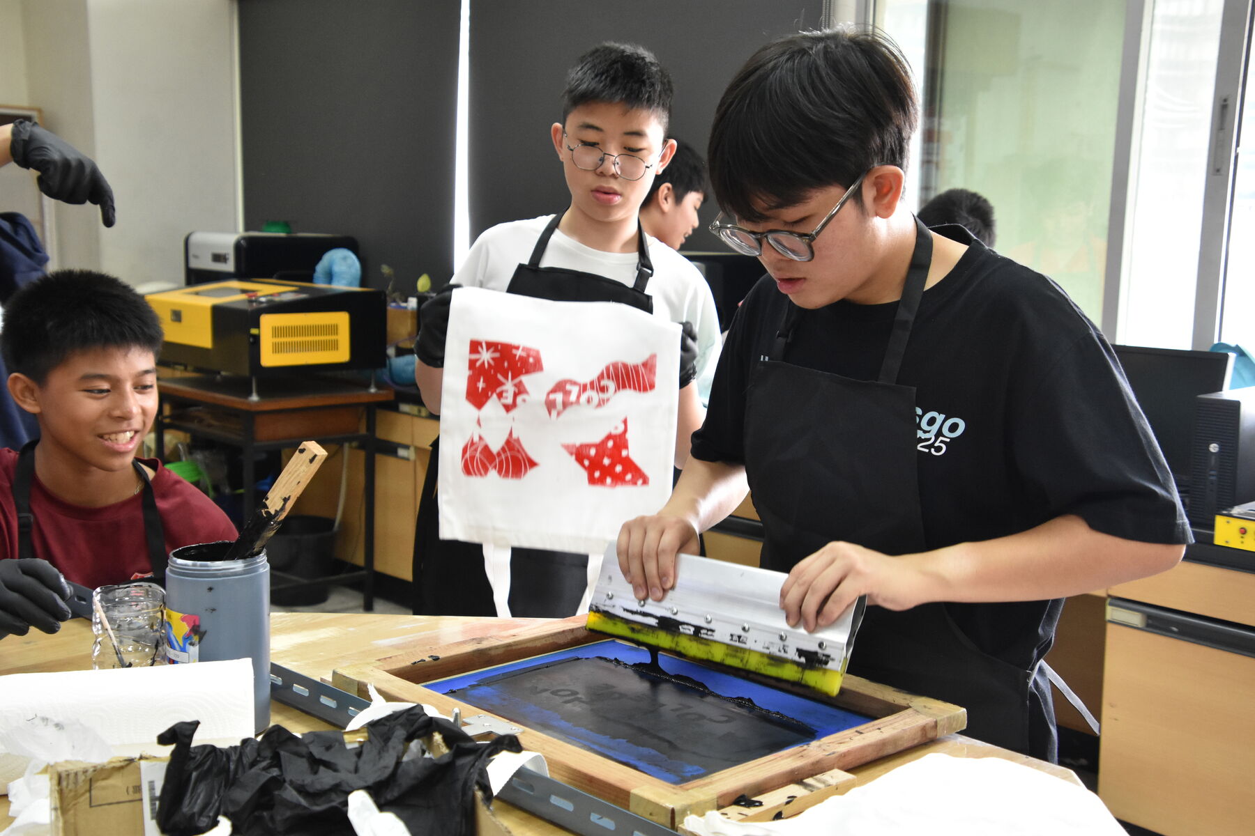 Pulling ink across a silkscreen, while a freshly printed tote is held up behind